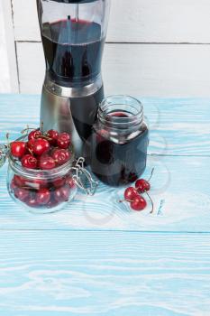 Cherry juice with glass jar,of berries, blender and juice on blue wooden background