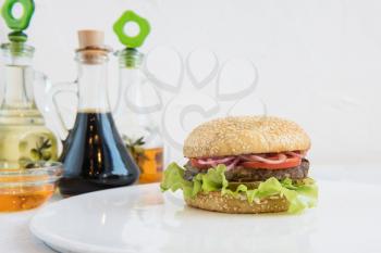 Tasty classical burger with meat cheese lettuce onion, tomato and sauce on white table