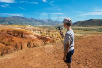 Teen boy recording video on phone in valley of Mars landscapes in the Altai Mountains, Kyzyl Chin, Siberia, Russia