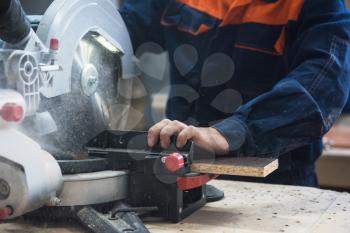 Furniture production or craft concept: worker sawing the wood surface of furniture part with saw machine