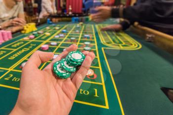 Casino, gambling and entertainment concept - male hand with stack of poker chips on a green table background