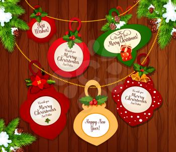 Christmas and New Year greeting cards hanging on xmas tree branches with holly berry, bell, ribbon bow and poinsettia flower on wooden background. Winter holidays festive poster design