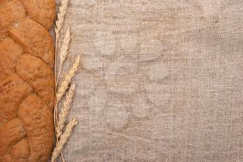 Wheat ears and bread on burlap background