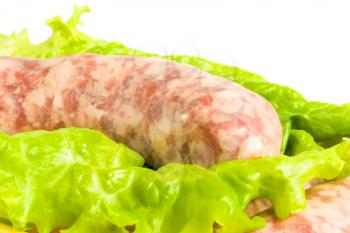 Closeup of one Uncooked Sausage on salad leaf over white