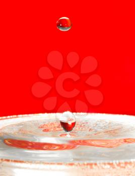 Extreme close-up. Falling droplets of water over red.