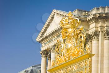 Golden crown over the gate and Palace in Versailles over blue sky. France