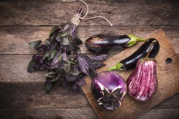 Aubergines and basil on chopping board and wooden table. Rustic style and autumn food photo