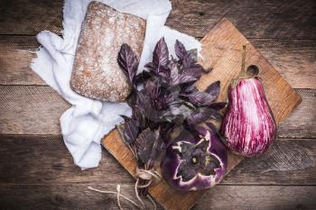 Aubergines, basil and bread on chopping board and wood. Rustic style and autumn food photo