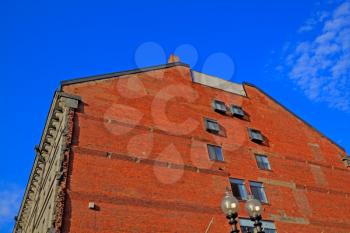 Red brick building wall with windows against the bright blue summer sky.