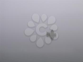 Lone fisherman with a fishing rod in a boat on the river in a fog
