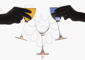 Two hands pouring different colored cocktails into a wine glass