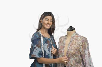 Female fashion designer trying a dress on a mannequin and smiling
