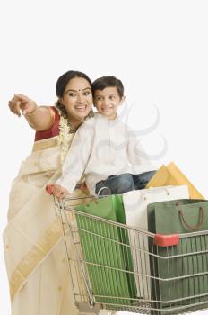 Woman pointing forward with her son standing on a shopping cart