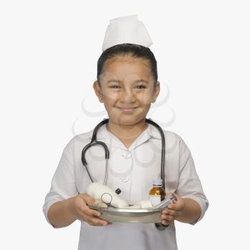 Girl dressed as a nurse and holding a tray of medicines and smiling