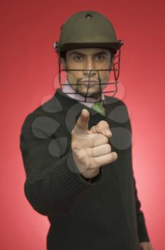 Portrait of a businessman wearing a cricket helmet and pointing