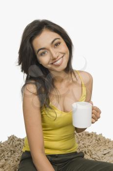 Woman sitting on a rug and holding a cup of coffee