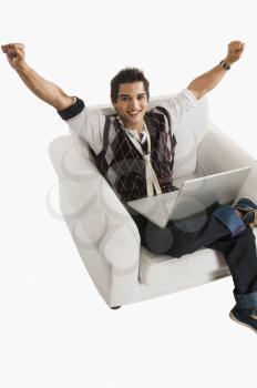 Portrait of a man cheering while using a laptop