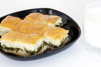 Pieces of spinach pie with cheese on black dish and glass of yogurt