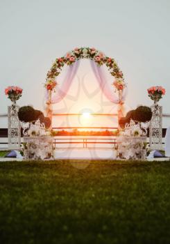 Wedding ceremony by the river at sunset. Arch decorated with flowers in the center of the composition