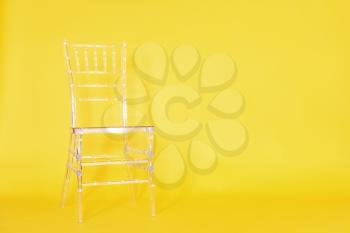 Transparent plastic chair on a yellow background in a photo studio.