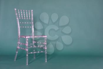 Transparent plastic chair on a green background in a photo studio.