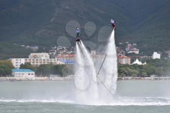Beautiful show on the water, sports team fly on flyboards in the sea against the background of the mountains