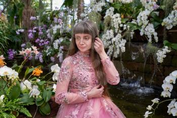 Young girl in a pink fashionable dress among the many orchids in a special winter indoor garden