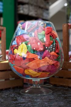 Large glass vase in the shape of a wine glass with new multi-colored balloons inside for a choice in the store.