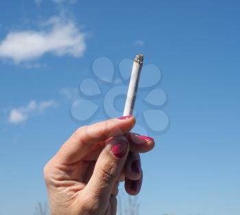 female hand holding cigarette against blue sky