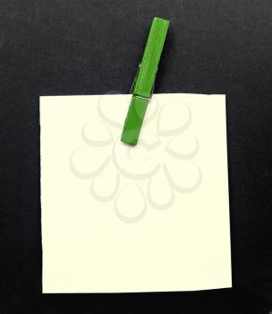 A blank notepad over a black background with a green clothespin
