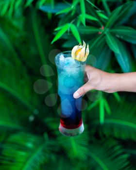 Woman holding blue colored cocktail with green background