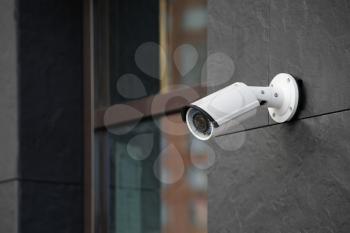 Modern CCTV camera on wall of building outdoors�