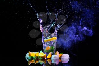 Glass with splashing water and slices of lemon on black background�