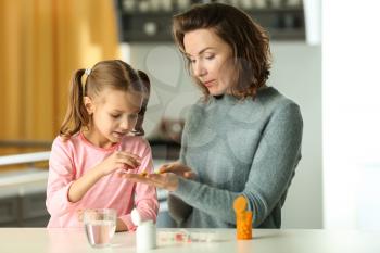 Young woman giving pill to her daughter at table�