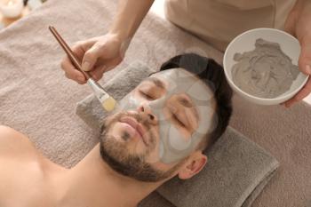Cosmetologist applying cosmetic mask on man's face in spa salon�