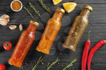 Composition with bottles of different sauces and vegetables on wooden background, flat lay�