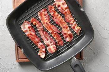 Grill pan with tasty bacon on wooden board�