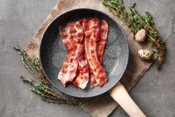 Frying pan with tasty bacon on grey background�