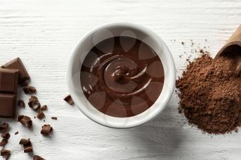 Bowl with molten chocolate on wooden background�