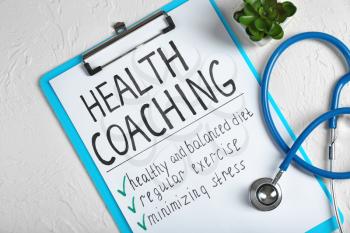 Health coaching written on sheet of paper with stethoscope on white textured background�