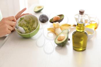 Woman making nourishing mask with avocado in kitchen�