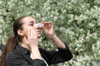 Young woman using eye drops near blooming tree. Allergy concept�