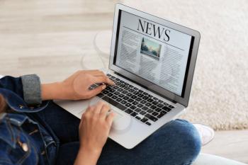 Woman reading news on laptop screen at home�