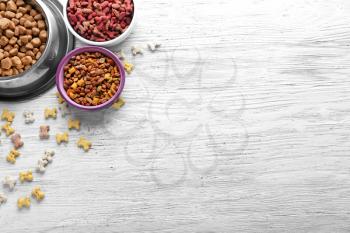 Bowls with pet food on wooden background�