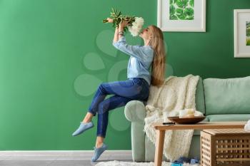 Attractive young woman with beautiful flowers sitting on sofa at home�