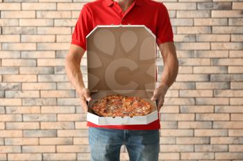 Young man holding box with tasty pizza against brick wall. Food delivery service�