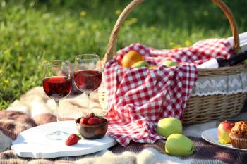 Basket with food and glasses of wine on plaid prepared for romantic picnic in park�