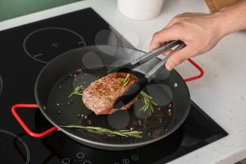 Man frying meat on pan in kitchen�