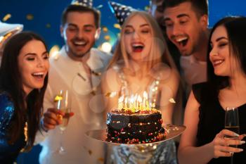 Young woman with tasty cake and her friends at birthday party in club�