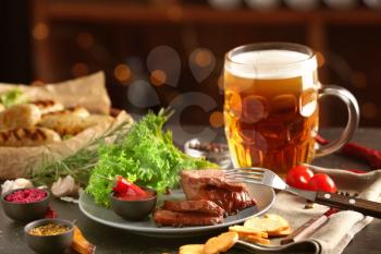 Mug of delicious beer with grilled steak and sauce on table�